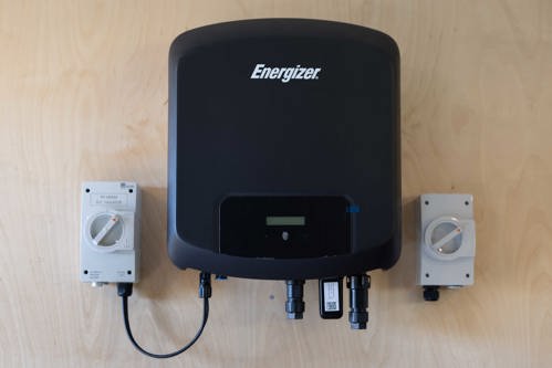 Energizer home battery storage unit mounted on a plywood wall, with electrical isolator switches and connecting cables on either side.