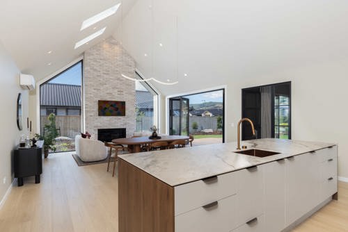 Open plan kitchen and living area with porcelain benchtop, brick fireplace and high raking ceilings – David Reid Homes Nelson show home, Richmond